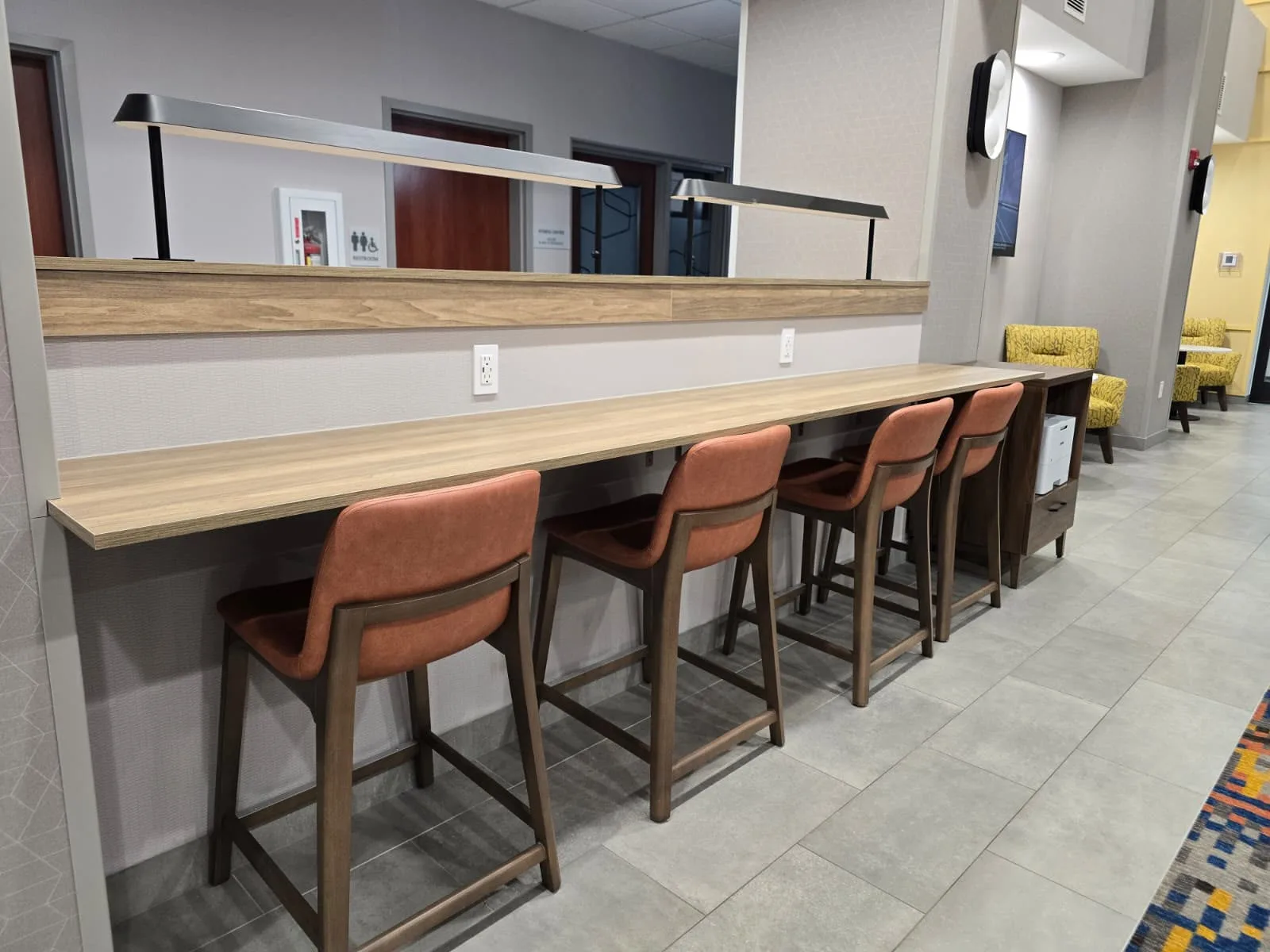 Long wall-mounted work counter with chairs, power outlets, mirrors, and linear task lights.